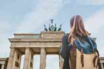 A tourist girl with a backpack looking at the Brandenburg Gate in Berlin